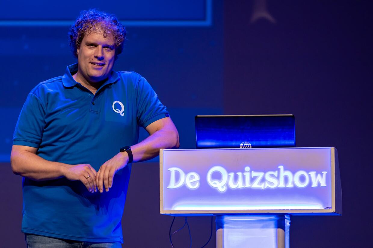 Bouke Koning naast de lessenaar van De Quizshow, in blauw podiumlicht
